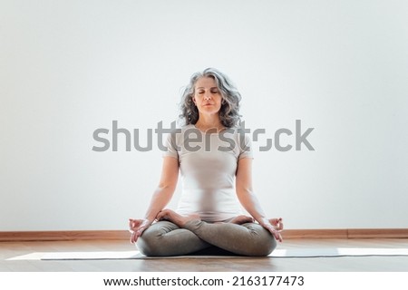 Full length view of the elderly woman practicing yoga at lotus pose in studio. Mature yoga teacher is take time for herself at home