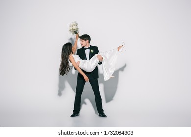 full length view of elegant bridegroom holding african american bride on hands on white background