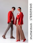 full length view of fashionable couple in red blazers and sunglasses looking at camera  on grey