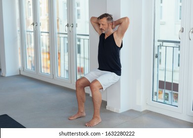 Full length view of a fit middle-aged man exercising wall sit during indoor workout for legs muscles - Powered by Shutterstock