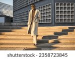 Full length view of multiracial man in casual style trench coat standing at street stairs