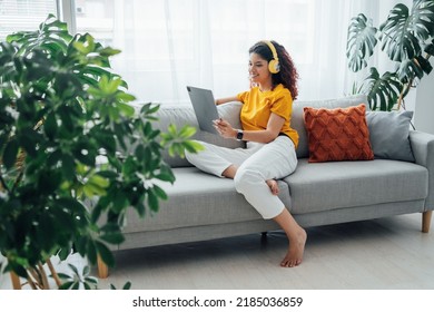 Full length view of the multiracial woman wearing headphones distance learning at home. Student girl using a tablet in a bright room with plants 