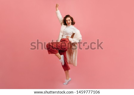 Full length view of pleased young lady in coat. Studio shot of positive girl fooling around on pink background.