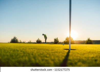 Full length view of the silhouette of a male player, hitting a long shot on the putting green of a professional golf course of a modern country club