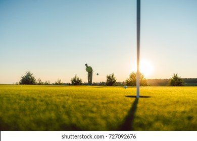 Full length view of the silhouette of a male player hitting a long shot on the putting green, of a professional golf course of a modern country club