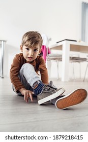 Full Length View Of Small Cute Caucasian Boy Little Child Kid Sitting On The Wooden Or Laminated Vinyl Floor At Home Putting On Or Taking Off The Shoes In Day Alone Front View