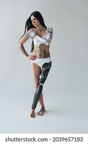 Full Length View Of The Tattooed Woman With Artificial Leg And Cyber Body Art Posing At The Studio. Unusual Appearance Concept. Stock Photo