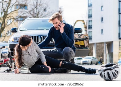 Full length view of a worried young driver calling the ambulance after hitting and injuring accidentally a female bicyclist on a city street 