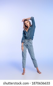 Full Length View Of Young Barefoot Woman In Denim Shirt And Jeans Posing On Blue