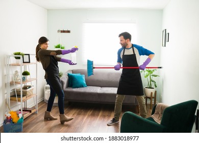 Full Length View Of A Young Couple Role Playing And Looking Ready To Fight With Some Cleaning Products At Home