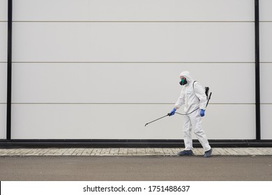 Full length wide angle portrait of one worker wearing protective gear and spraying chemicals outdoors during disinfection or cleaning, copy space - Powered by Shutterstock