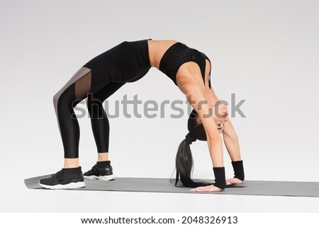 full length of woman in black sportswear doing handstand bridge on fitness mat on grey