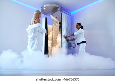Full length woman entering freezing booth at the cosmetology clinic. Female taking cryotherapy treatment with beautician standing at the capsule door.