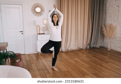 Full length of woman standing in Tree pose practicing yoga leading healthy lifestyle preparing body for childbirth during morning training in light apartment - Powered by Shutterstock