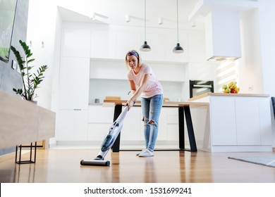 Full Length Of Worthy Caucasian Blonde Housewife Using Steamer To Clean Floor In Living Room.