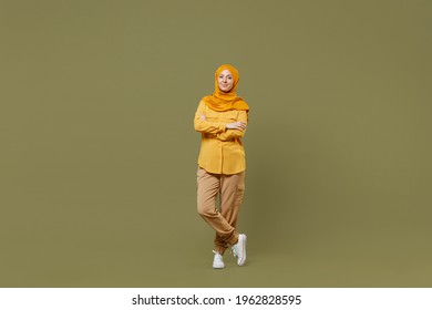 Full length young arabian asian muslim woman in abaya hijab yellow clothes hold hands crossed folded isolated on olive green khaki background studio. People uae middle eastern islam religious concept