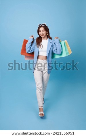 Full length young asian shopper woman walking and holding shopping bag feeling happy excited for discount promotion isolated on blue background.