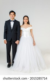 Full Length Of Young Attractive Asian Couple, Soon To Be Bride And Groom, Woman Wearing White Wedding Gown. Man Wearing Black Tuxedo, Standing Together. Concept For Pre Wedding Photography.