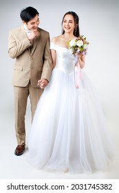 Full length of young attractive Asian couple, man wearing beige suit, woman wearing white wedding gown standing together holding hands. Concept for pre wedding photography.