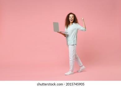 Full Length Young Black African Fun Happy Smiling Curly Student Woman In Blue Shirt Hold Laptop Pc Computer Do Winner Gesture Clench Fist Celebrating Isolated On Pastel Pink Background Studio Portrait