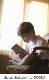 Full length of young boy reading book on chair at home