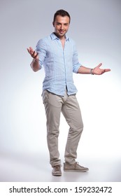 full length of a young casual man welcoming you with his arms wide open and a smile. on gray background