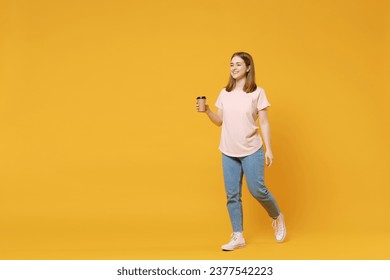 Full length of young caucasian student woman 20s wearing casual basic pastel pink t-shirt, jeans hold in hand paper cup of tea drinking coffee walk going isolated on yellow background studio portrait - Powered by Shutterstock