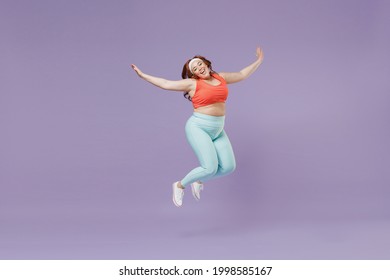 Full length young chubby overweight plus size big fat fit woman wear red top warm up training jump high with outstretched hands isolated on purple background home gym. Workout sport motivation concept