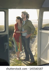 Full Length Of Young Couple Embracing On Beach View Through Campervan Door