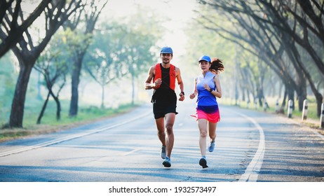 Full length of young couple in sport clothing running through the tree tunnel street together
