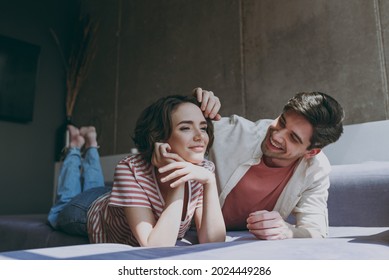 Full length young couple two friends woman man in casual clothes lying on sofa watch tv movie caring tender boyfriend touch girlfriend hair rest indoors at home flat together People lifestyle concept