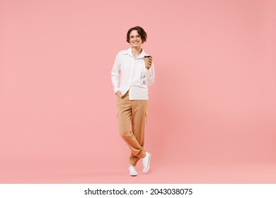 Full length young employee business woman corporate lawyer in classic formal white shirt work in office hold takeaway delivery craft paper brown cup coffee to go isolated on pastel pink background.