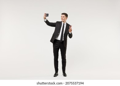 Full length young employee business corporate lawyer man in classic formal black grey suit shirt tie work in office do selfie shot mobile phone show victory v-sign gesture isolated on white background