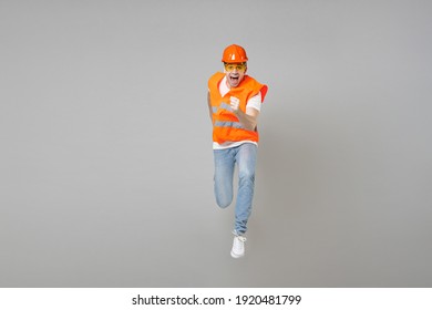 Full length of young employee handyman sporty fast man in orange vest protective hardhat jump high running isolated on grey background studio. Instruments for renovation apartment. Repair home concept