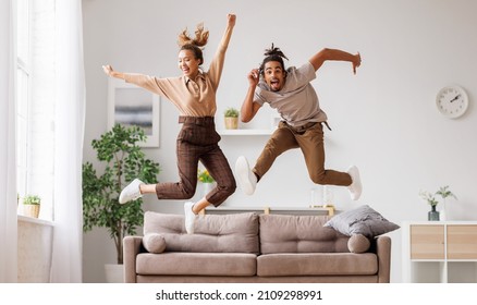 Full length of young energetic active african american family couple jumping on sofa in cozy living room, carefree black man and woman have fun together at home. Freedom and happiness in relationship - Powered by Shutterstock