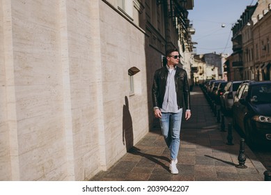 Full length young excited tourist trendy fun cheerful positive happy man 20s wearing black leather jacket eyeglasses strolling in city downtown outdoors look aside. Concept of people urban lifestyle. - Powered by Shutterstock