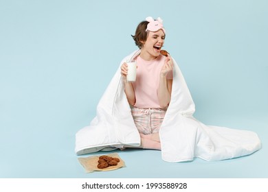 Full Length Young Excited Woman 20s In Pajamas Jam Sleep Eye Mask Rest At Home Wrap Cover Blanket Duvet Sit Cookie Milk Eat Drink Isolated On Pastel Blue Background Studio Good Mood Breakfast Concept