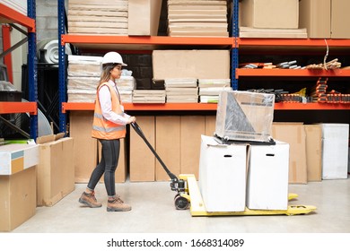 Full length of young female Hispanic employee pushing cardboard boxes on trolley by rack in factory - Powered by Shutterstock