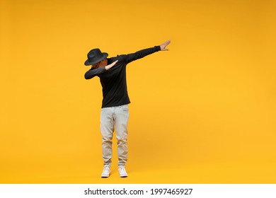 Full length young fun african man 20s wear stylish black hat shirt eyeglasses doing dab hip hop dance hands move gesture youth sign hiding covering face isolated on yellow background studio portrait.