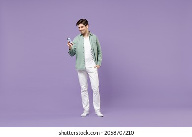 Full Length Young Fun Caucasian Man 20s In Casual Mint Shirt White T-shirt Using Mobile Cell Phone Chat Online In Social Network Isolated On Purple Background Studio Portrait People Lifestyle Concept