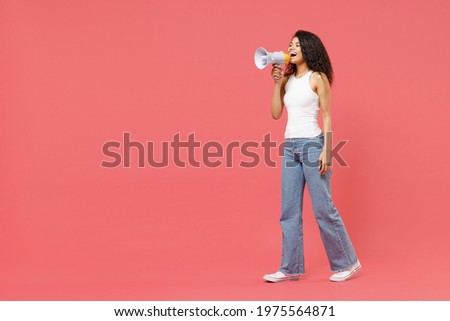 Full length young fun expressive excited happy curly african american woman 20s in white tank shirt screaming shouting loudly hot news in megaphone isolated on pink color background studio portrait
