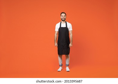 Full Length Young Fun Man 20s Barista Bartender Barman Employee In Black Apron White T-shirt Work In Coffee Shop Looking Camera Isolated On Orange Background Studio . Small Business Startup Concept