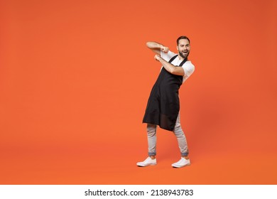 Full Length Young Fun Man Barista Bartender Barman Employee In Black Apron White T-shirt Work In Coffee Shop Do Winner Gesture Clench Fist Isolated On Orange Background Studio Small Business Startup