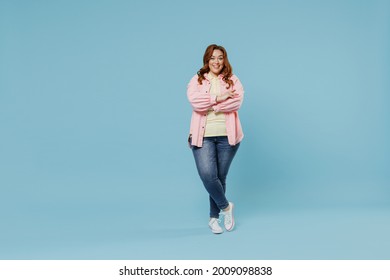 Full Length Young Fun Smiling Redhead Chubby Overweight Woman 30s With Curly Hair Wear In Pink Shirt Jeans Casual Clothes Hold Hands Crossed Folded Isolated On Pastel Blue Background Studio Portrait.