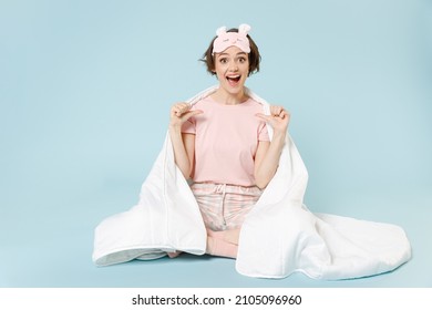 Full length young fun woman in pajamas jam sleep eye mask rest at home sit wrap cover blanket duvet point fingers on herself isolated on pastel blue background studio Good mood night bedtime concept