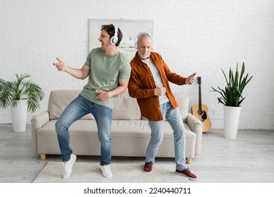 full length of young guy with senior dad in wireless headphones listening music and dancing in living room - Shutterstock ID 2240440711