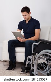 Full Length Of Young Handicapped Man Using Digital Tablet While Sitting On Sofa At Home