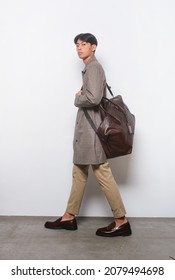 Full Length Young Handsome Businessman 
 Man Wearing Striped, Long Coat And Khaki Pants With Brown Handbag  Walking On Gray Background In Studio,
