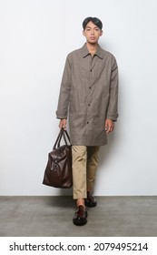 Full Length Young Handsome Businessman 
 Man Wearing Striped, Long Coat And Khaki Pants With Brown Handbag  Walking On Gray Background In Studio,
