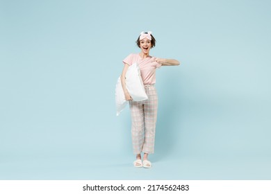 Full length young happy fun woman 20s in pajamas jam sleep eye mask rest relax at home point index finger on pillow isolated on pastel blue color background studio. Good mood night bedtime concept.